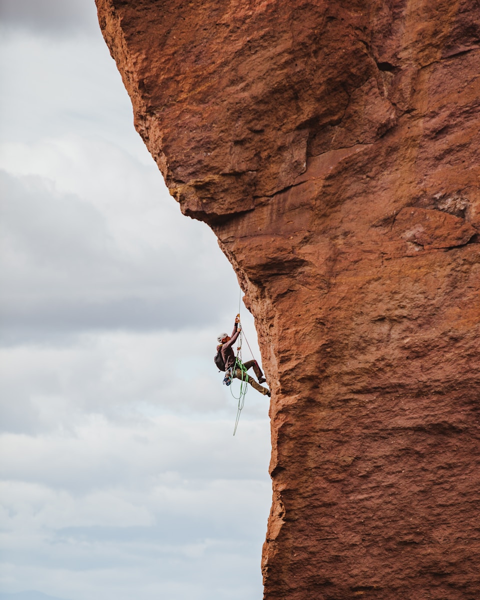 Photo by Sean Benesh man in black shorts climbing brown rock formation during daytime